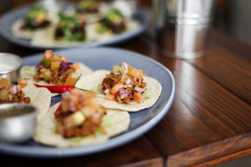 Small Mexican tortilla with meat and vegetables, bowl of sauce on a blue plate, on a dark wooden...