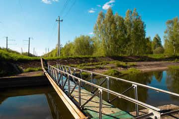 Pleasant summer landscape: old blue sky and clouds, green grass and a river lake artificial channel and an old industrial bridge.