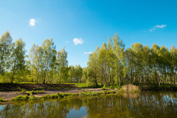 Fototapeta na wymiar Pleasant summer landscape: old blue sky and clouds, green grass and a river lake artificial channel. A happy idyllic scenery view.