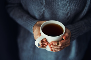 Cozy home. Female hands holding hot cup of coffee or tea.