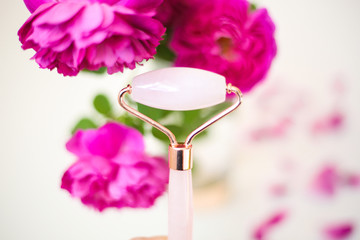 Pink quartz roller on floral background. Spa settings. Derma roller for anti aging. Beauty tools.