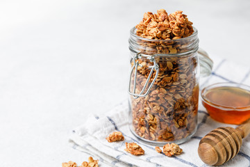 Homemade oatmeal granola in open glass jar on white background.