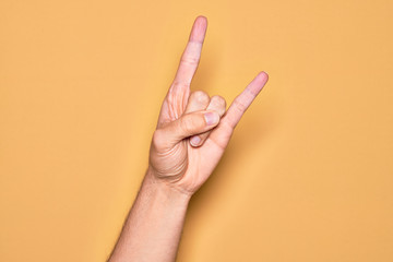 Hand of caucasian young man showing fingers over isolated yellow background gesturing rock and roll...