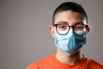 Ritratto di ragazzo giovane con occhiali da vista , maglia arancione e mascherina chirurgica ,...