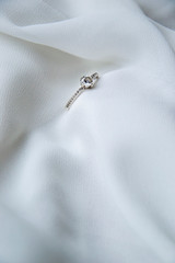Close up picture of engagement ring on white silky background as gently wallpaper background with empty space for text inviting card on weeding with small jewelry on the side as present to say yes 