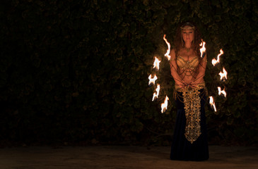 Belly dancer dressed in arabic clothes handling fire gadgets in the night in the middle of a landscape