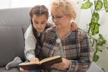 happy little girl and grandmother sit on couch and read book together