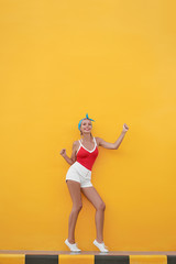 Summer vacation. Colorful studio portrait of happy young woman dancing against yellow wall.