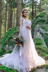 Happy bride in a pink wedding dress. The girl holds a wedding bouquet in her hands. Boho style wedding ceremony in the forest.