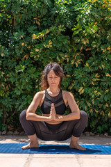 A woman in a tracksuit practicing meditation and yoga doing a  difficult position at home