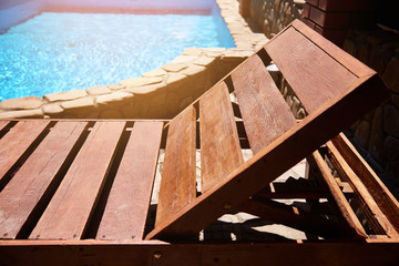 A wooden sunbed made of planks stands near the pool on a Sunny summer day. A wonderful holiday at home or in the country, a deep pool in the sun. Background and place for text