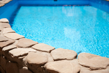 Obraz premium the large pool with clear blue water is perfect for relaxing at home. The deep pool is lined with decorative stone along the edge, the sun is reflected in the water.