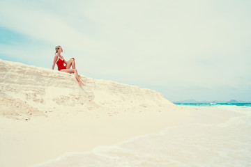Vacation on the seashore.Young woman in red swimsuit sitting on the beautiful tropical white sand beach.