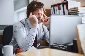 Middle-aged employee suffering from a headache on his workplace