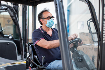 Operaio  con mascherina di protezione guida un carrello elevatore nel magazzino in cui lavora