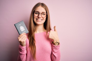 Fototapeta premium Beautiful redhead tourist woman holding canadian canada passport over pink bakcground happy with big smile doing ok sign, thumb up with fingers, excellent sign