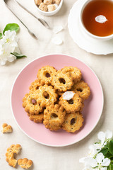 Shortbread in a pink ceramic plate on a light table. A plate of cookies on the table among the flowering trees. A plate full of cookies. Rustic homemade cakes. The view from the top