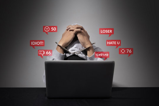 cyber bullying concept. A handcuffed man is accused of being a social defendant, bending his head in front of the laptop computer with hate speech as a cyber bullying popup message from social media.