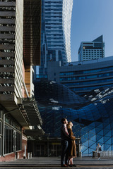 Fototapeta premium A young woman and a man hug, kiss and walk in the city center near skyscrapers.