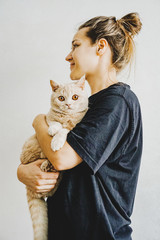 girl holds a frightened cat of British breed in her arms.