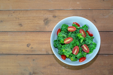Kale salad with tomato, healthy food, on wooden background.