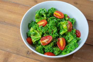 Kale salad with tomato, healthy food, on wooden background.