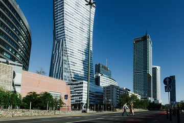 A young woman and a man cross the road in the city center near skyscrapers.