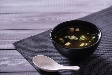 Japanese hot miso soup in a black bowl on the wooden table. Horizontal view from above