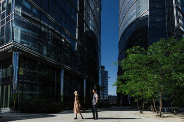 A beautiful woman and a man hug and walk in the city center near skyscrapers.