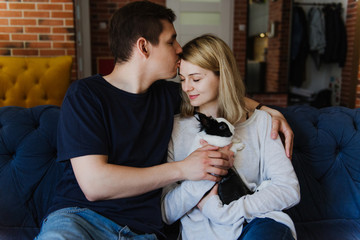 Beautiful woman and man hug, kiss and hold a rabbit in their arms while sitting on the bed.