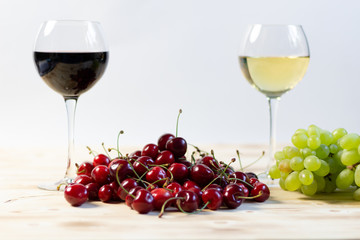 red wine glass with cherry berries and white wine glass with grape bunch on wooden background