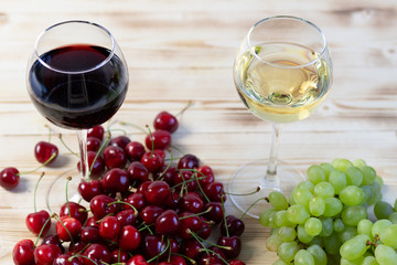 red wine glass with cherry  and white wine glass with grapes on wooden background