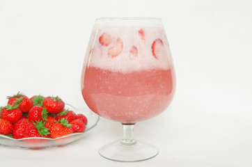 Strawberry cocktail in glass near a plate with fresh strawberries on white background