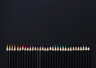 Colored pencil set arranged in line on black background. Stationery backdrop for your design