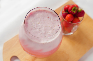 Strawberry cocktail or strawberry milkshake in glass near a cup of fresh trawberries on a wooden board