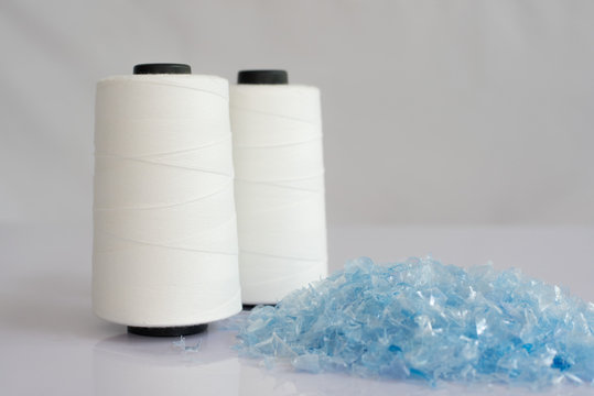 Bottle flake,PET bottle flake,Plastic bottle crushed,Small pieces of cut blue plastic bottles & Raw White Polyester FDY Yarn spool with white background