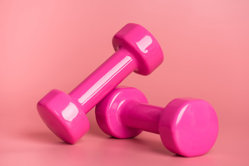 Workout concept. Close-up photo of two pink dumbbells isolated on pastel pink background