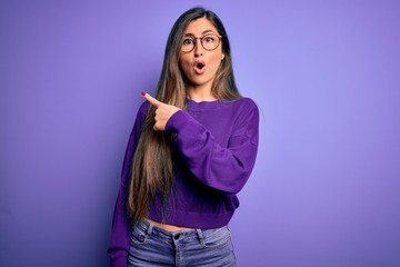 Young beautiful smart woman wearing glasses over purple isolated background Surprised pointing with finger to the side, open mouth amazed expression.