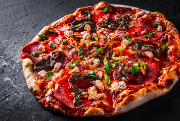Pizza with Mozzarella cheese, salami, chicken meat, beef, ham, Tomato sauce, pepper, spices. Italian pizza on Dark grey black slate background