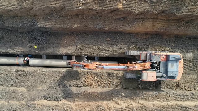 Drone above excavating bulldozer or tractor digging and land cleaning soil land. Men at work outdoor outside with heavy machinery loading arm installing water pipeline
