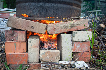 burning garbage in a barrel in nature. an iron barrel stands on bricks in which wooden boards burn. red flame. a lot of red hot coals with ash