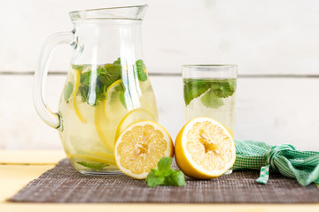 Lemonade with lemon and mint in a jug on a yellow rustic table.