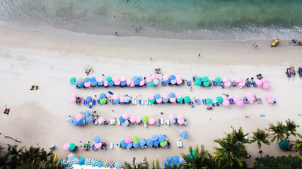 Aerial view of sandy beach with colorful umbrellas, People bathing in the sun.
