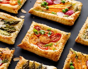 Puff pastry small tarts with addition of vegetables on a black background, top view