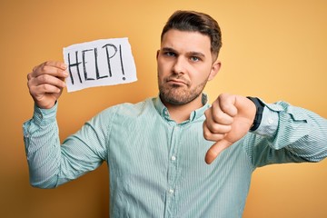 Young business man with blue eyes asking for help holding paper note over yellow background with...