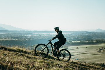 Fototapeta na wymiar Young athletic man on an e-bike pedaling up the hill with a beautiful view. Amazing nature for meditating, hiking, biking and exploring.