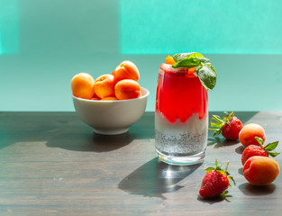 Bright red jelly in a glass and a bowl of apricots on the table, in the sunlight with space