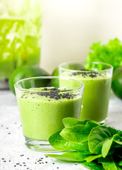 Green smoothie of avocado, spinach and seeds in glasses and spinach leaves on a gray concrete table. Healthy eating, raw food diet and vegan food. Green vegetables smoothie.