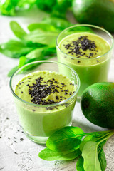 Green smoothie of avocado, spinach and seeds in glasses and spinach leaves on a gray concrete table. Healthy eating, raw food diet and vegan food. Green vegetables smoothie.