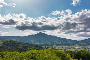 太陽光に照らされた大きな雲と新緑の里山